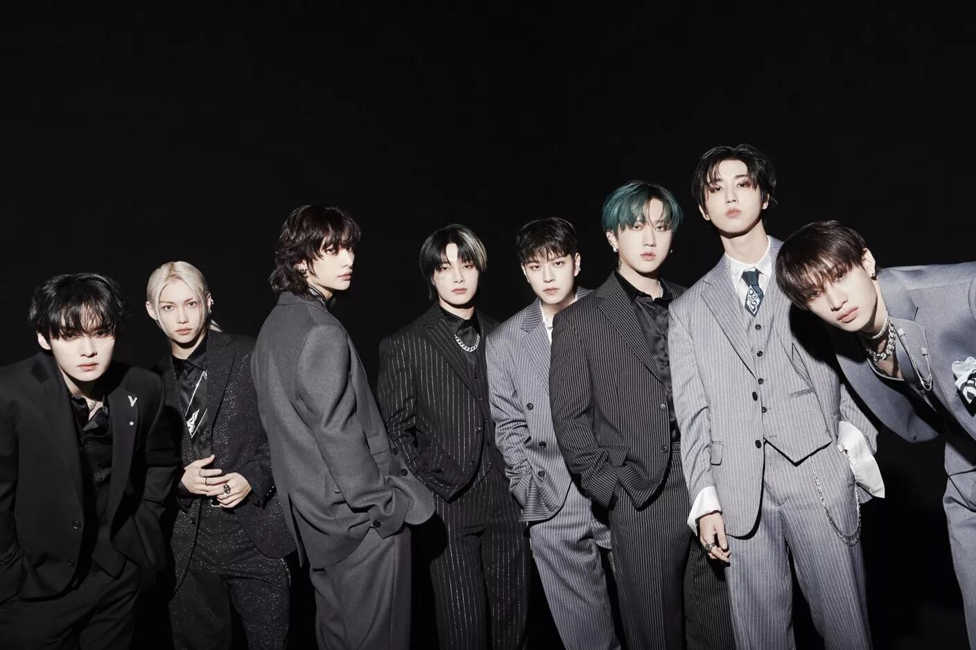 K-Pop boyband Stray Kids standing in a row in dark grey and black suits.
